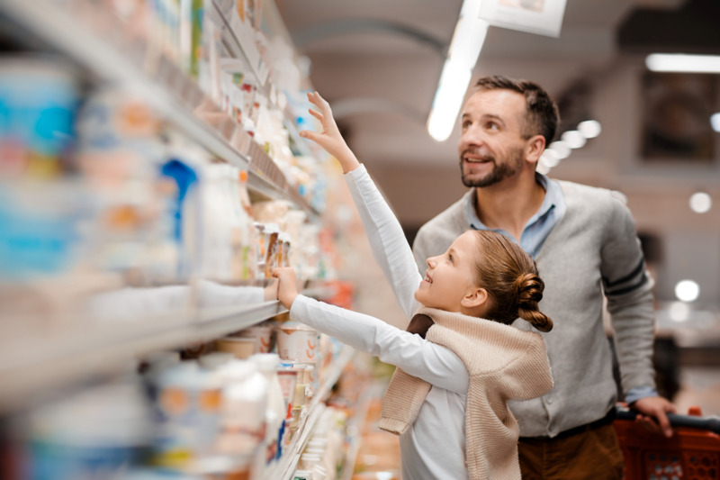 Mężczyzna i dziecko stoją przed ladą z produktami chłodniczymi w supermarkecie.